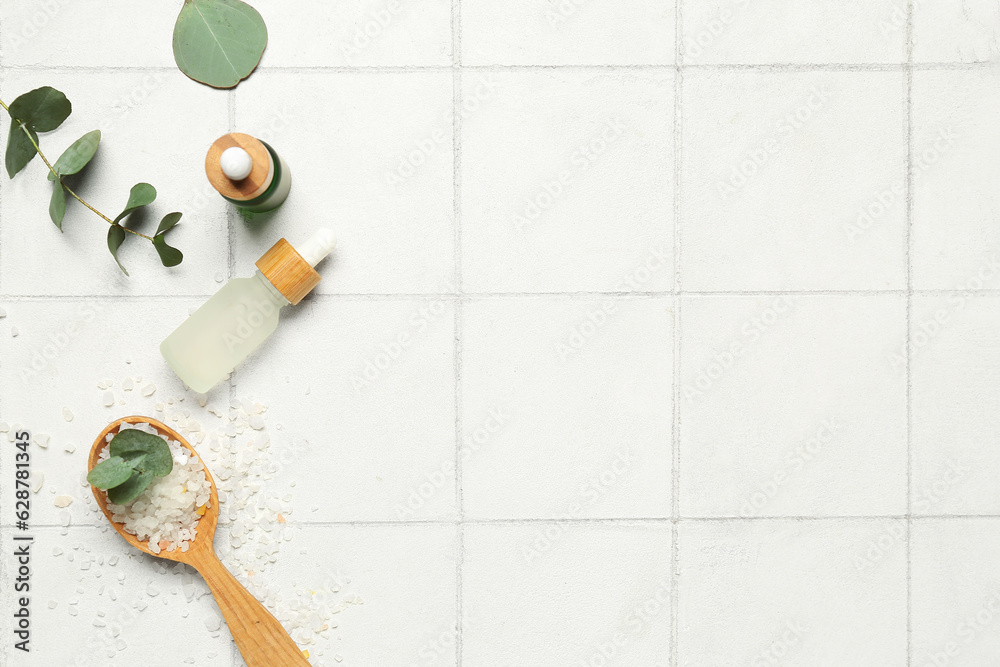 Cosmetic oil bottles with wooden spoon, eucalyptus branch and sea salt on tile background