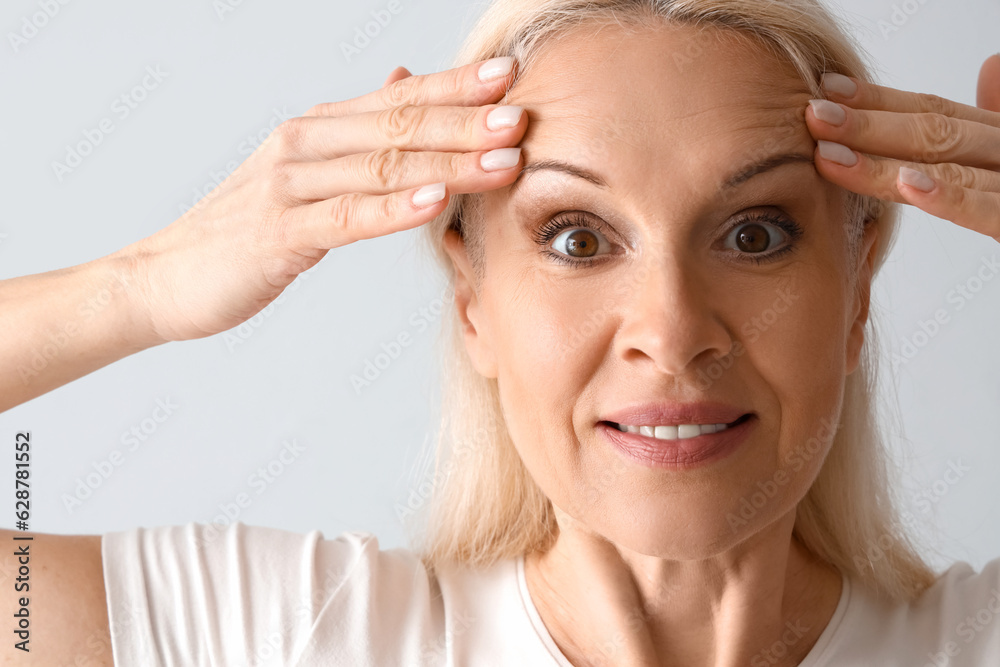 Mature woman doing face building exercise on light background, closeup