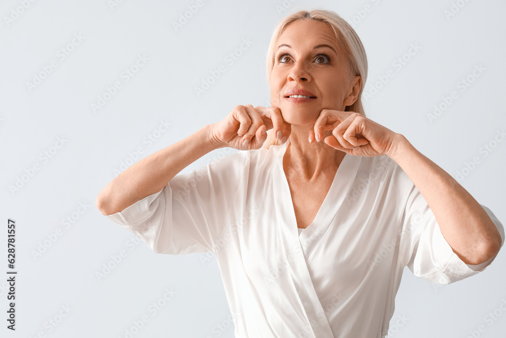 Mature woman doing face building exercise on light background