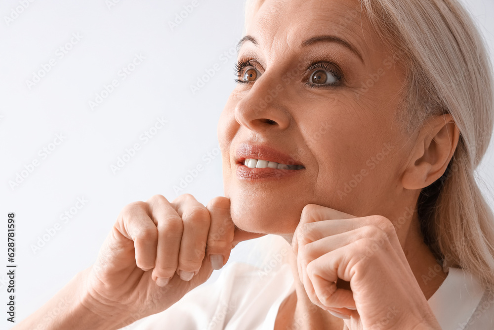 Mature woman doing face building exercise on light background, closeup