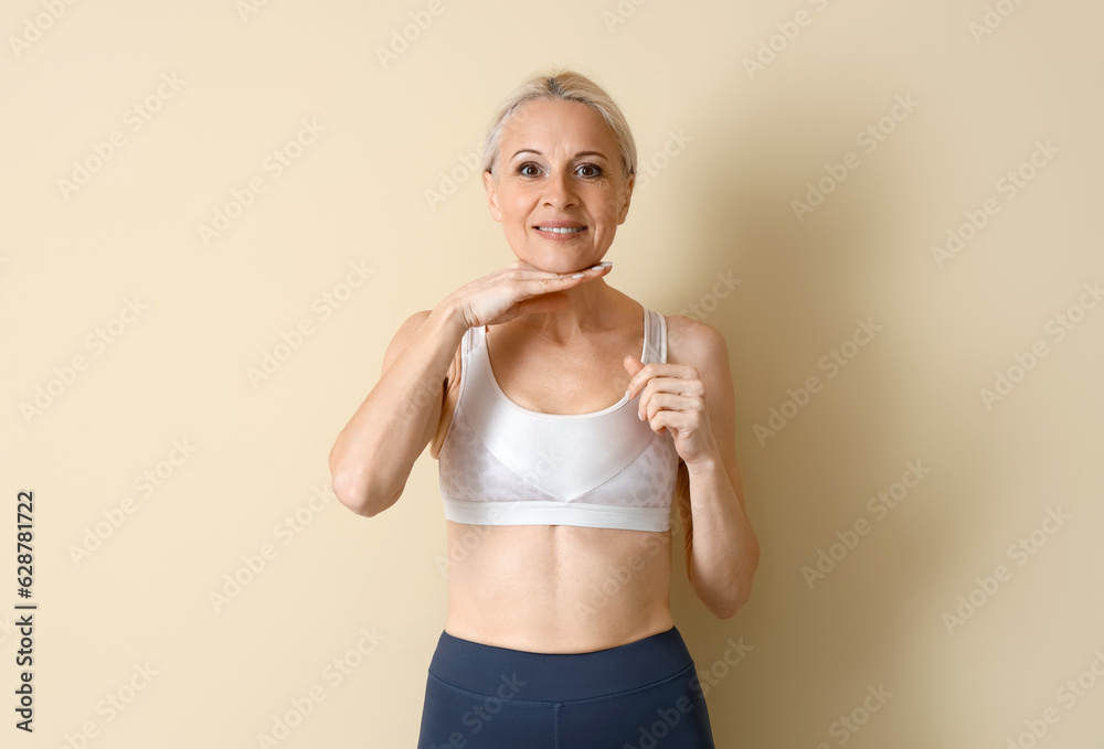 Sporty mature woman doing face building exercise on beige background