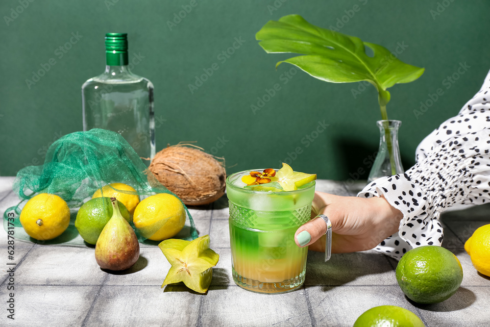 Woman holding glass of summer cocktail with carambola on tile table near green wall