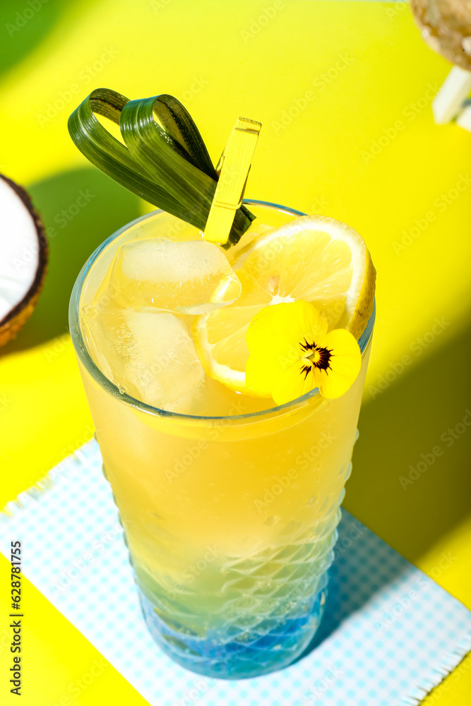 Fresh summer cocktail with lemon and flower on yellow table