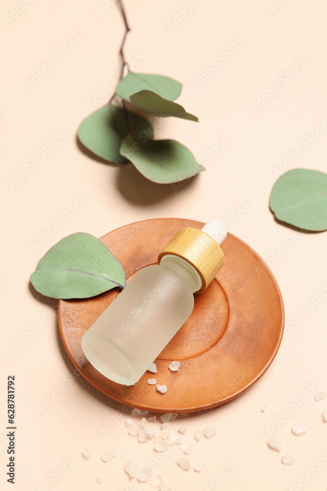 Bottle of cosmetic oil with sea salt and eucalyptus branch on beige background