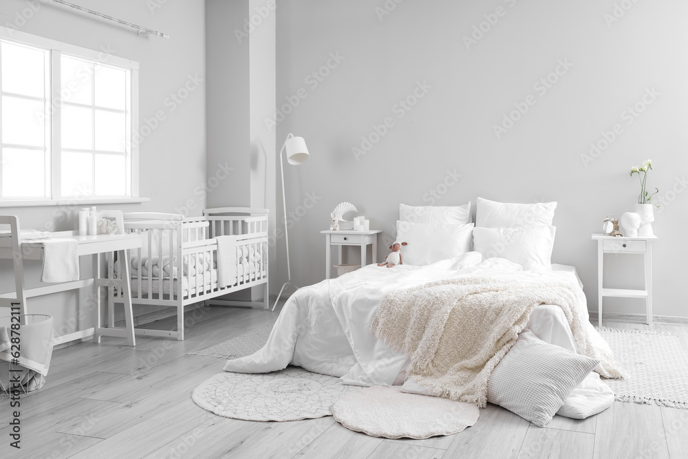 Interior of light bedroom with bed, changing table and baby crib