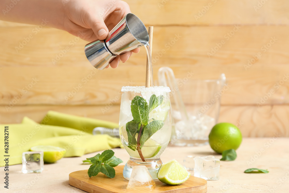 Female bartender making tasty mojito cocktail on table near wooden wall