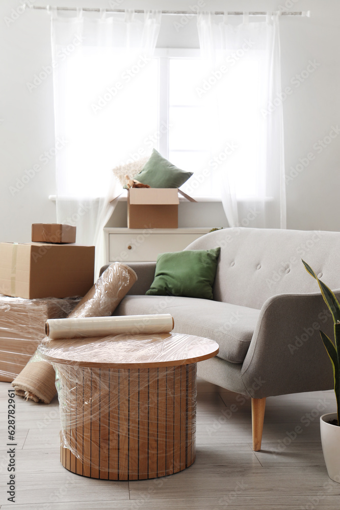 Sofa with wrapped table and cardboard boxes in living room on moving day