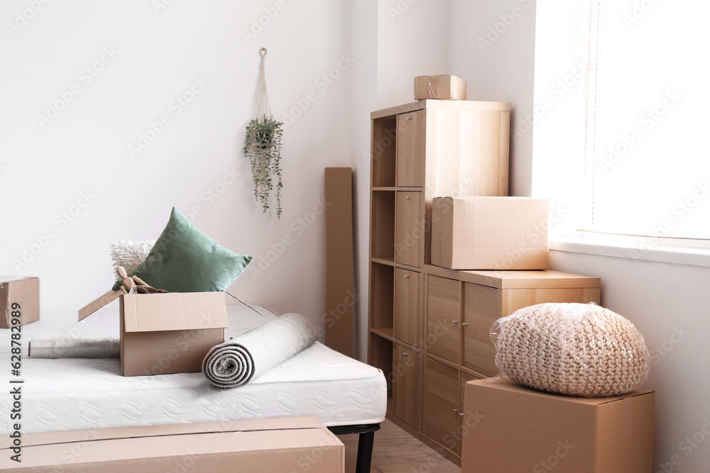 Bed with cardboard box and rolled carpet in room on moving day