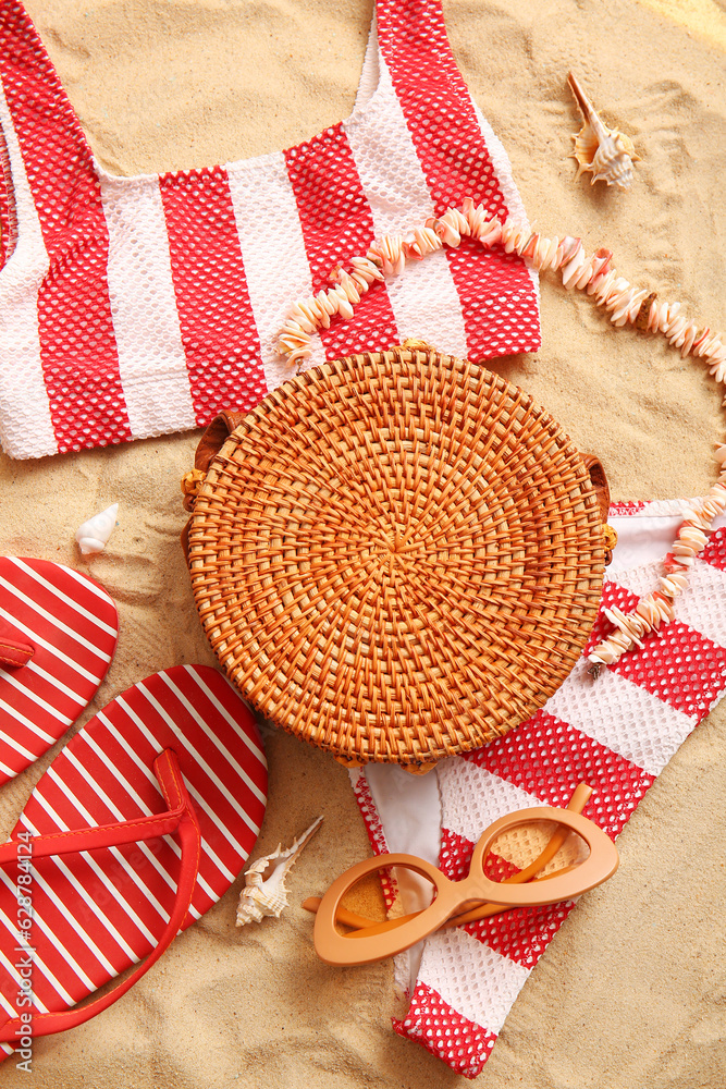 Stylish bag with swimsuit and different accessories on sand