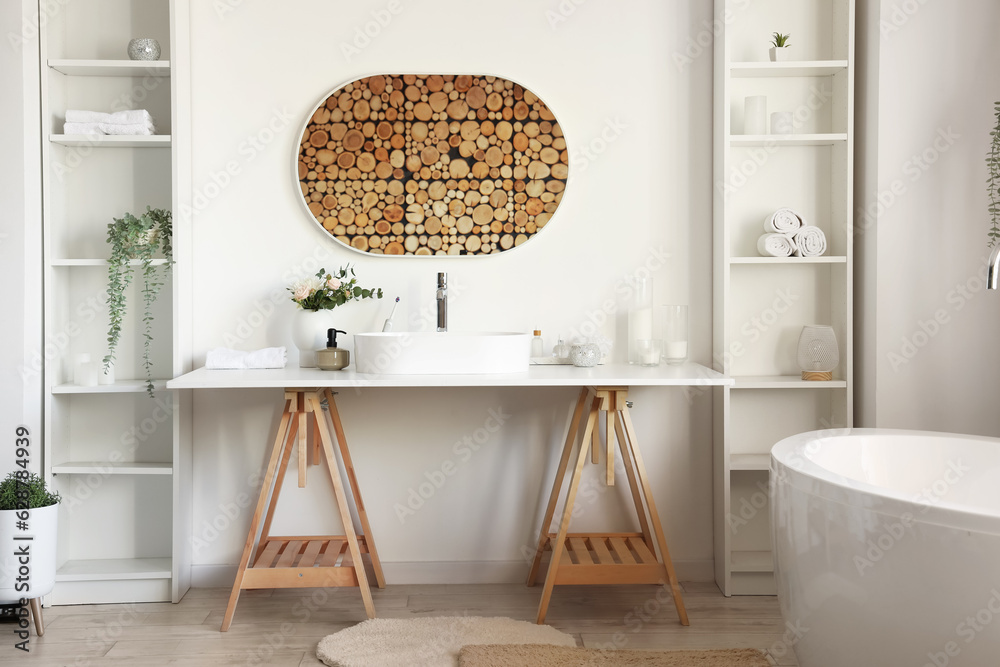 Interior of light bathroom with white sink, bathtub and shelving units