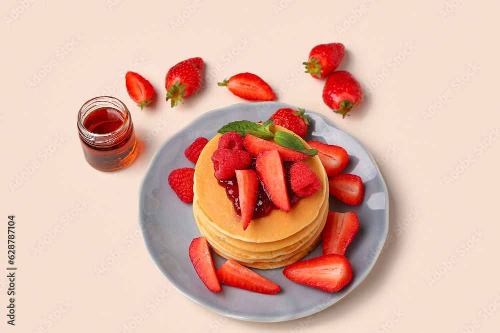 Plate with sweet pancakes, berries and jam on beige background