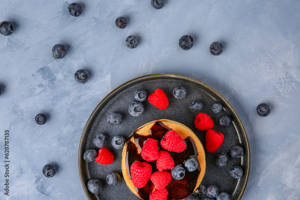 Plate with tasty pancakes and berries on blue background