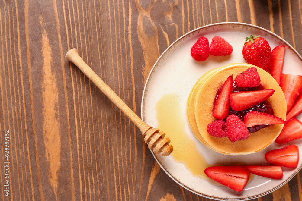 Plate with sweet pancakes, honey and berries on wooden background