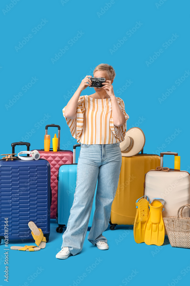 Mature woman with photo camera and suitcases on blue background