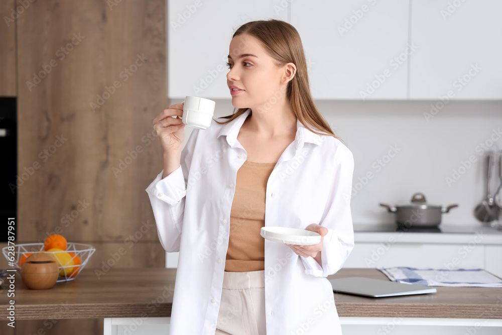 Happy young woman enjoying cup of coffee in modern kitchen