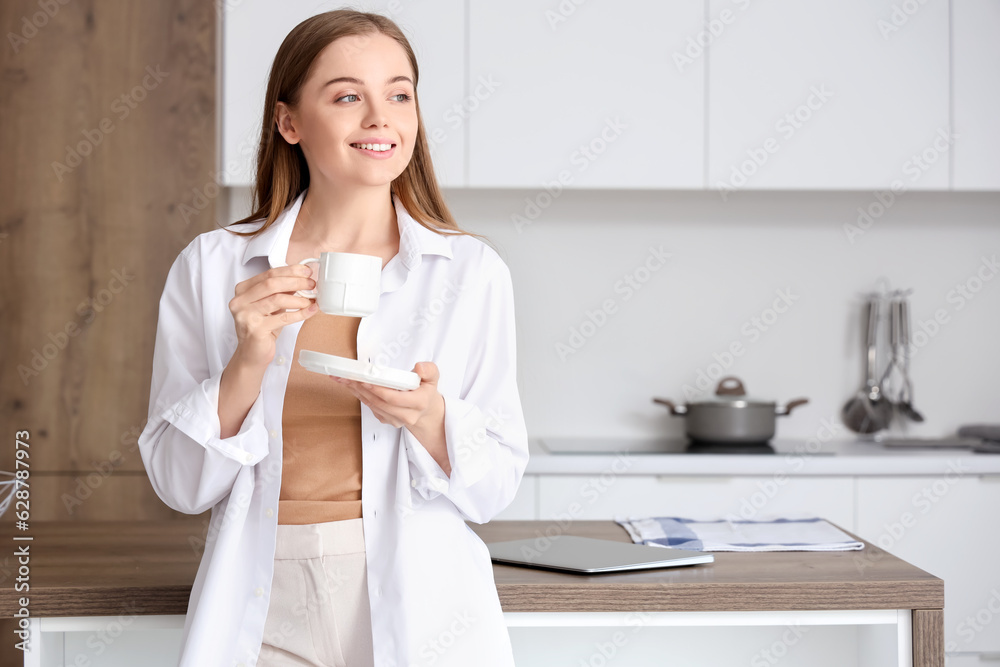 Happy young woman enjoying cup of coffee in modern kitchen