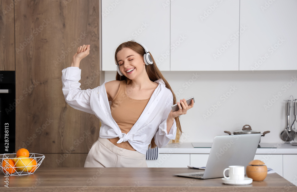 Happy young woman listening to music and dancing in modern kitchen