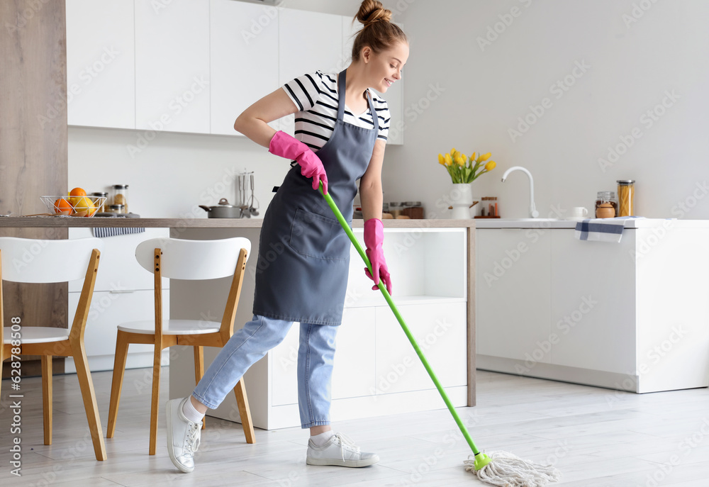 Pretty young woman mopping floor in light kitchen