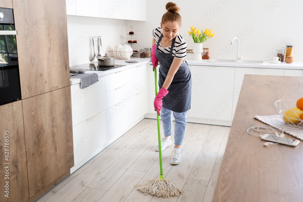 Pretty young woman mopping floor in light kitchen