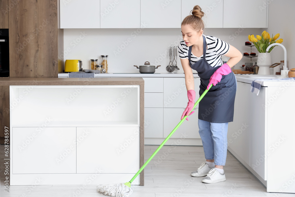 Pretty young woman mopping floor in light kitchen