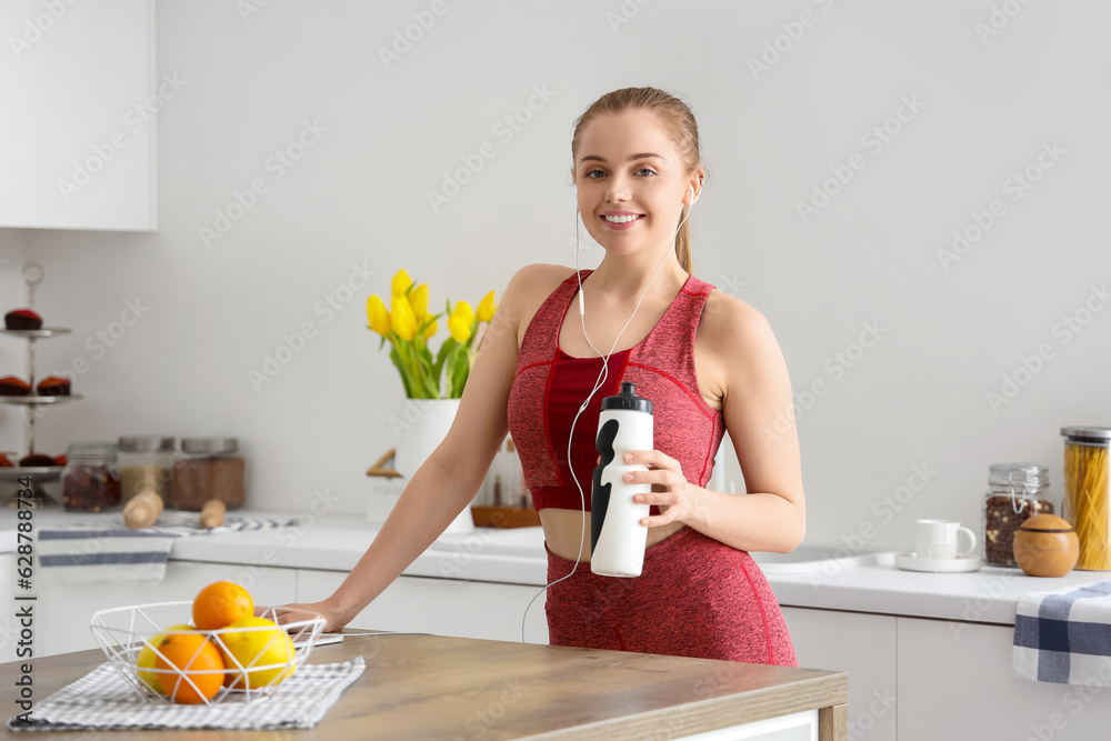 Sporty young woman with bottle of water in light kitchen