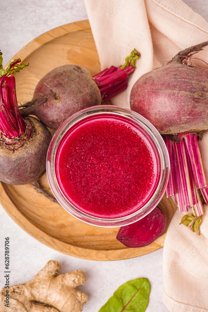 Glass of fresh beetroot juice and vegetables on light background