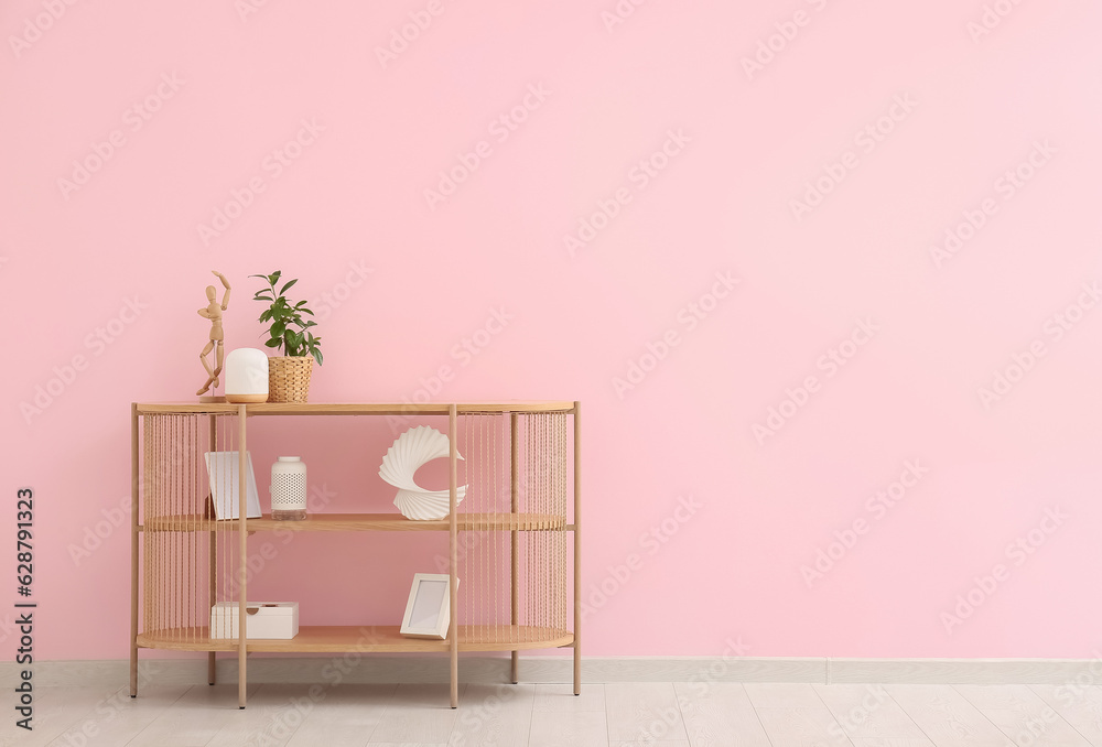 Modern shelving unit with houseplant and decor near pink wall in room