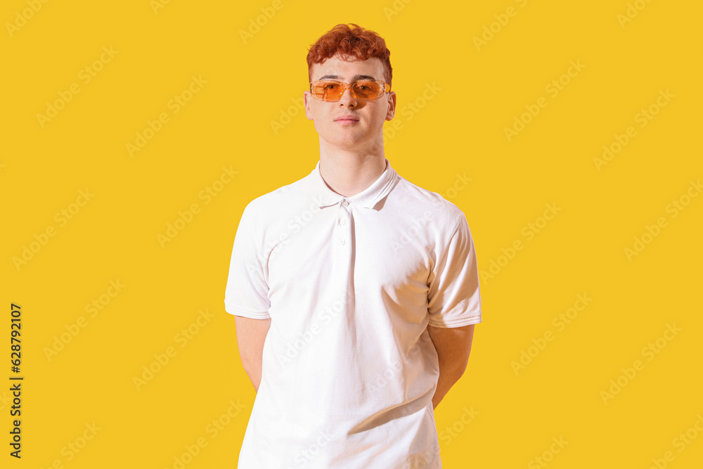 Young redhead man in stylish sunglasses on yellow background