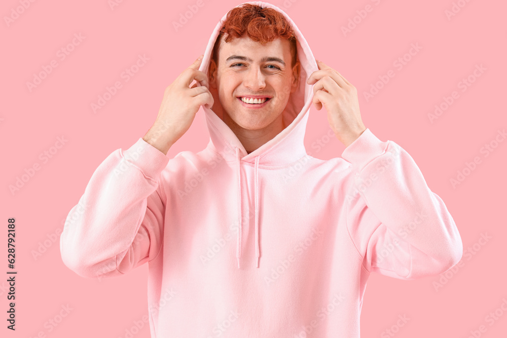 Young redhead man in hoodie on pink background