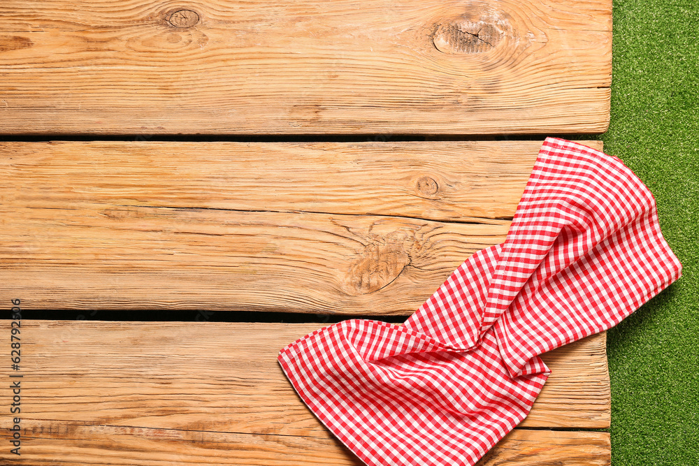 Red checkered napkin on wooden table against green grass background, closeup