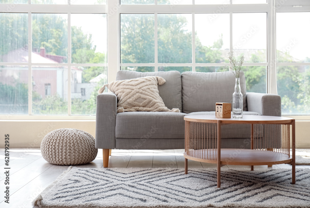 Interior of light living room with grey sofa, coffee table and large window