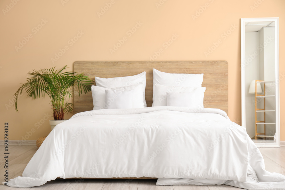 Comfortable bed with white pillows, mirror and houseplant in bedroom