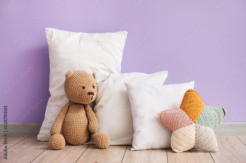 White pillows with teddy bear near lilac wall