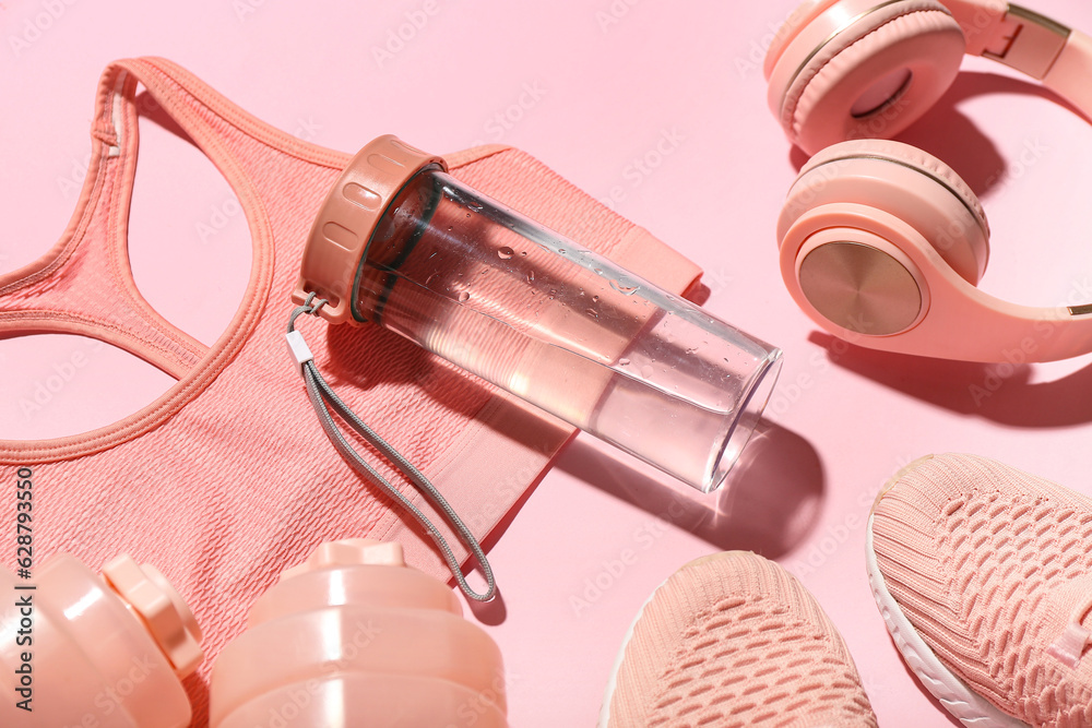 Composition with bottle of water, sports bra and headphones on color background, closeup