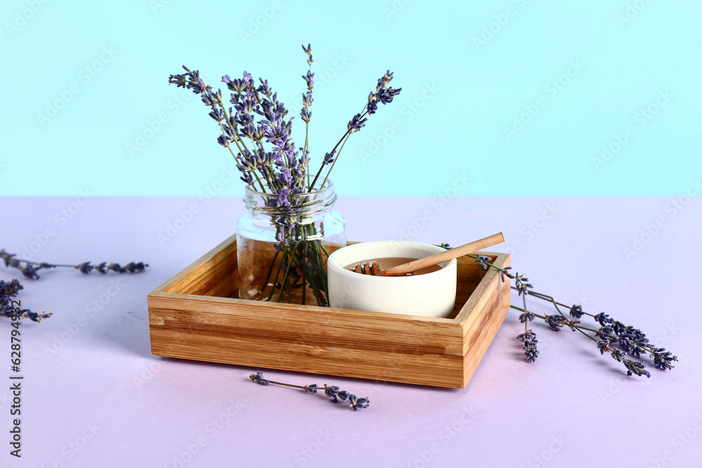 Wooden box with bowl of sweet lavender honey and flowers on lilac table