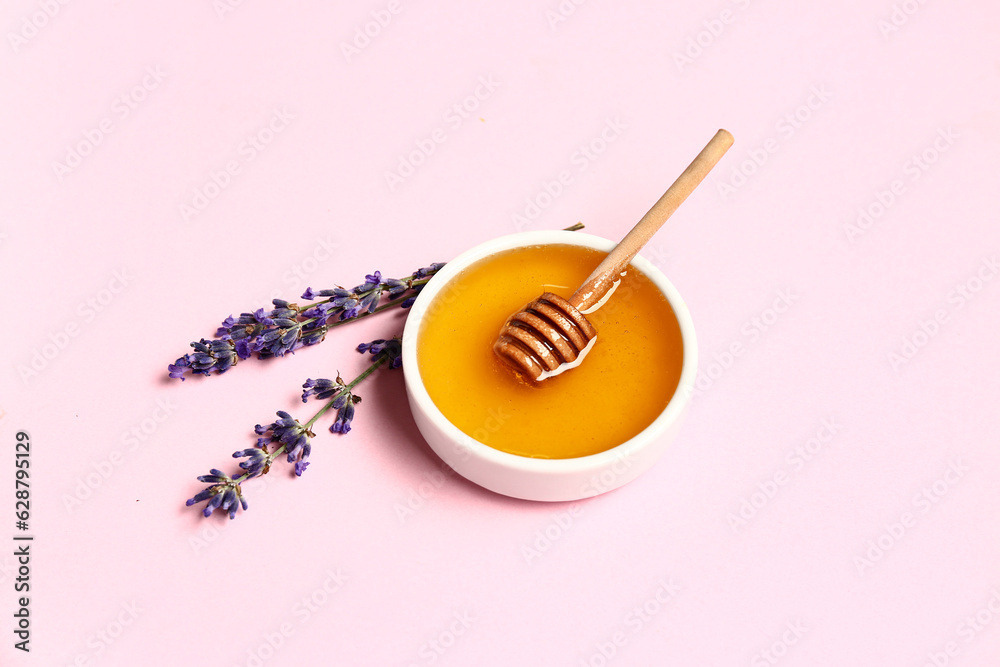 Bowl of sweet lavender honey, dipper and flowers on pink background