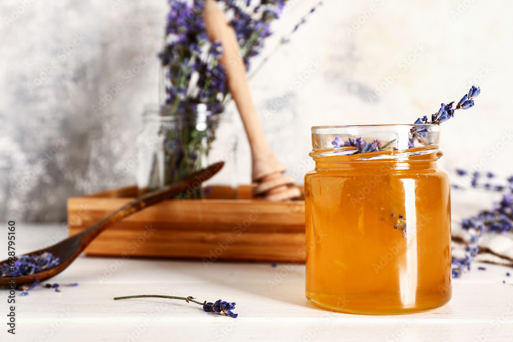 Jar of sweet lavender honey and flowers on white wooden table