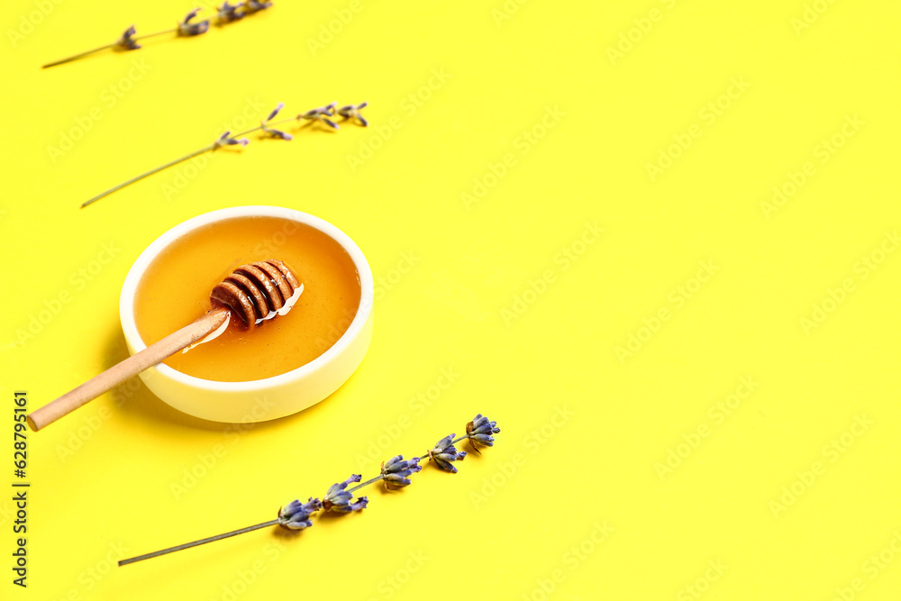 Bowl of sweet lavender honey, dipper and flowers on yellow background