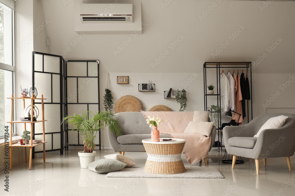 Interior of light living room with comfortable grey sofa, armchair and coffee table