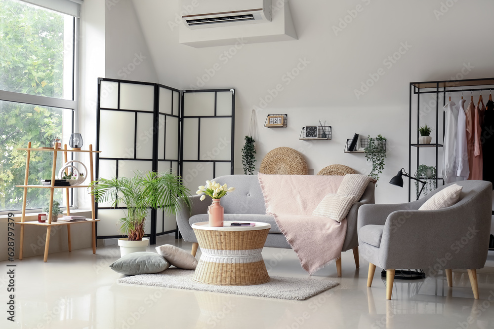 Interior of light living room with comfortable grey sofa, armchair and coffee table