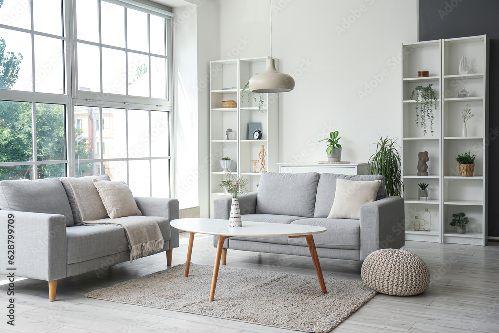 Interior of light living room with cozy grey sofas, coffee table and big window