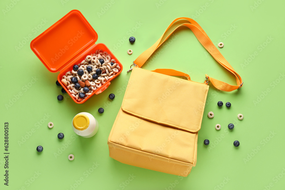 Bag with lunch box and bottle of milk on green background