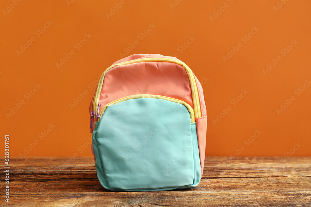 Colorful school backpack on wooden table near orange wall