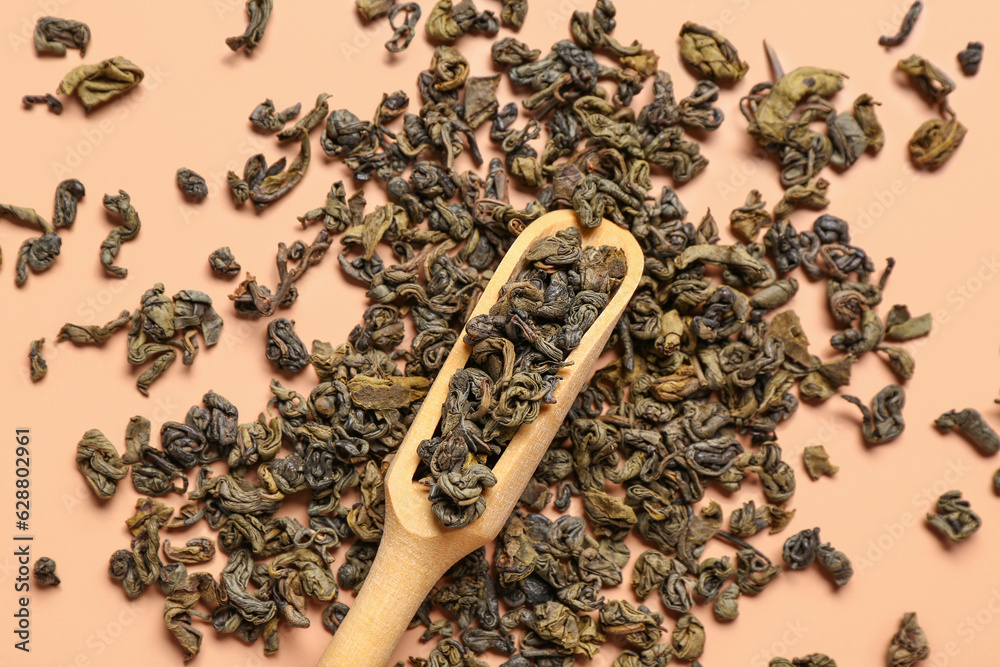 Wooden scoop with dry tea leaves on orange background