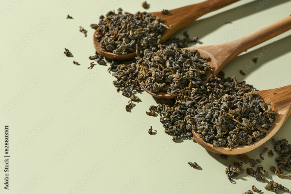 Wooden spoons with dry tea leaves on green background