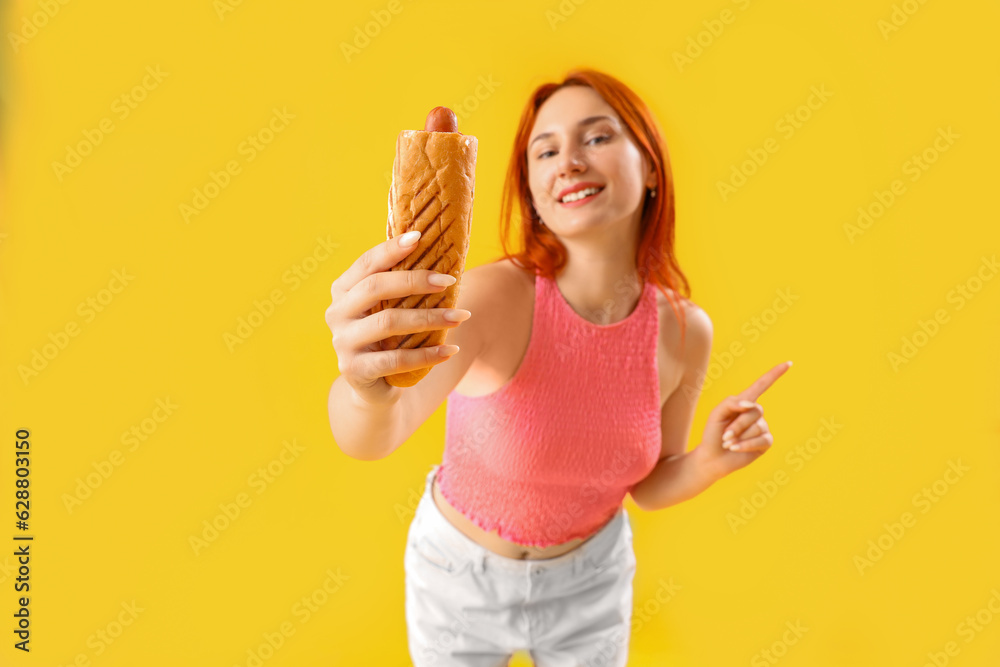 Beautiful young woman with tasty french hot dog on yellow background