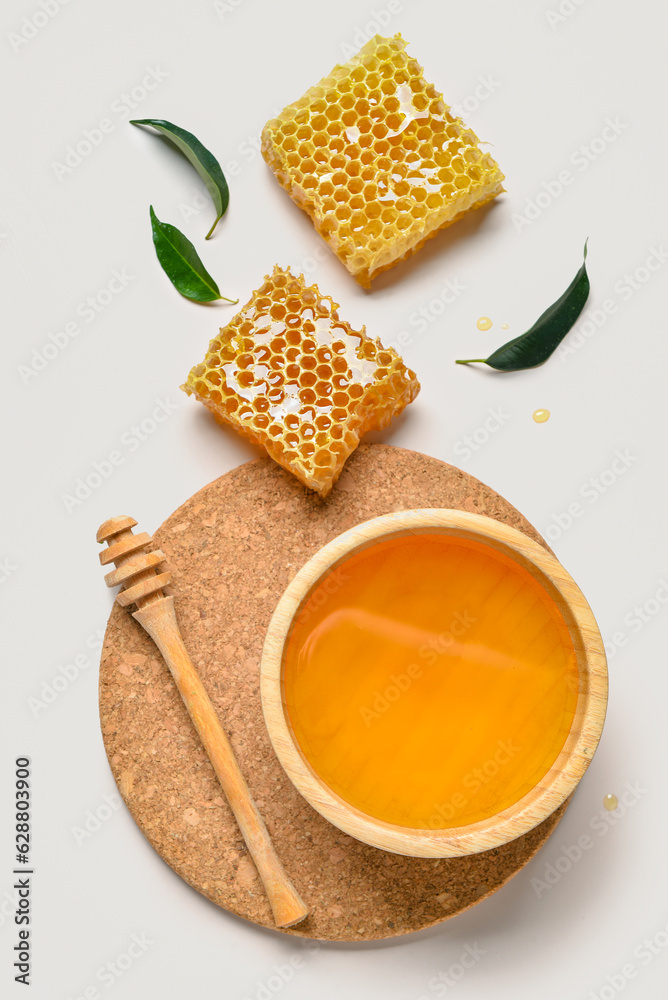 Bowl with sweet honey and combs on grey background