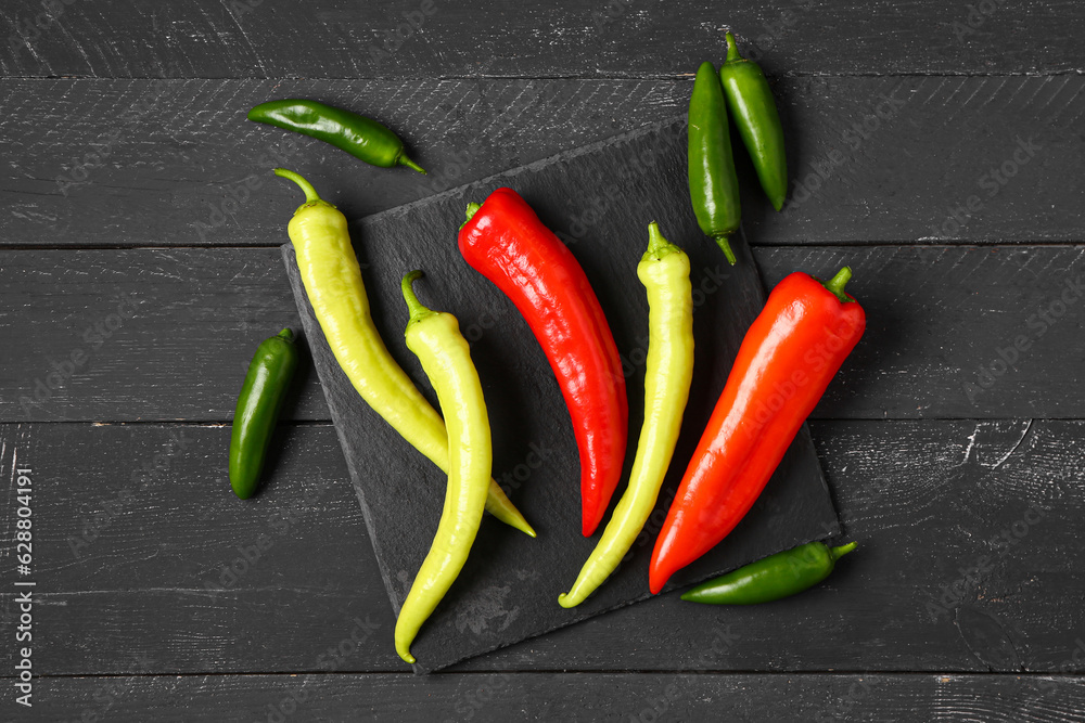 Board with different fresh chili peppers on black wooden background