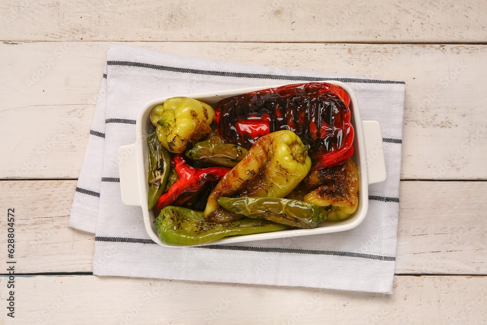 Baking dish with different grilled peppers on light wooden background