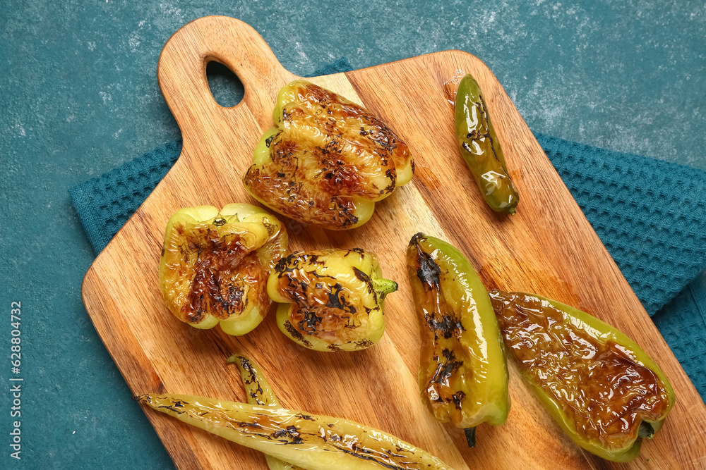 Wooden board with different grilled peppers on blue background